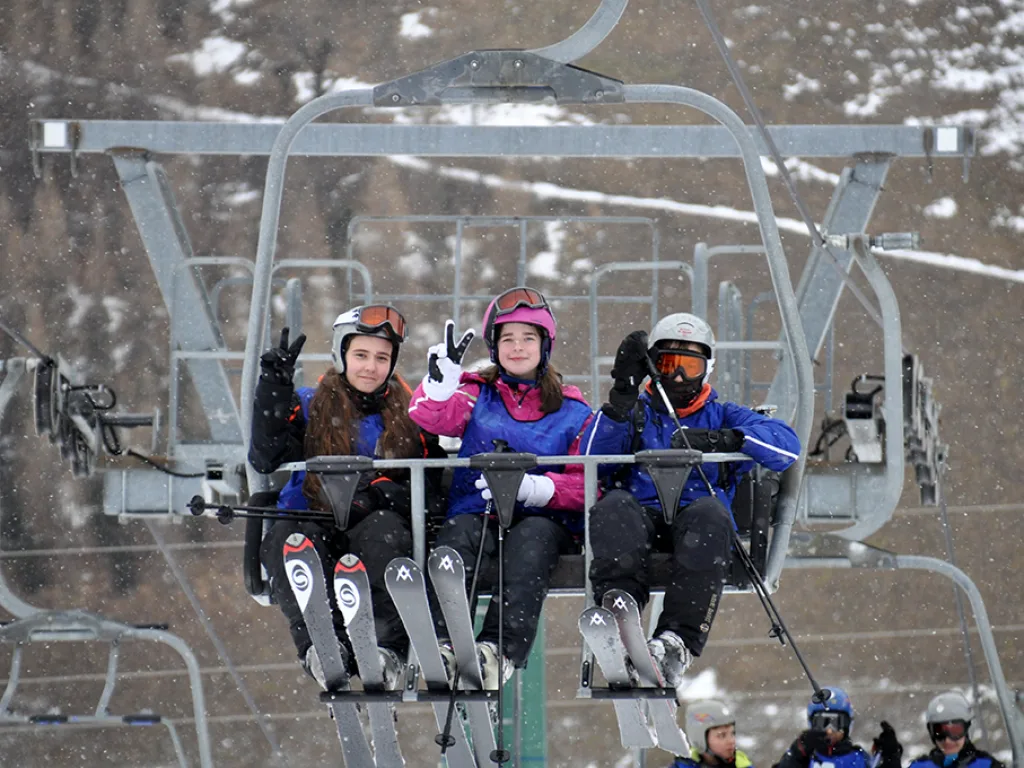 Drei Jugendliche im Sessellift über der Piste.